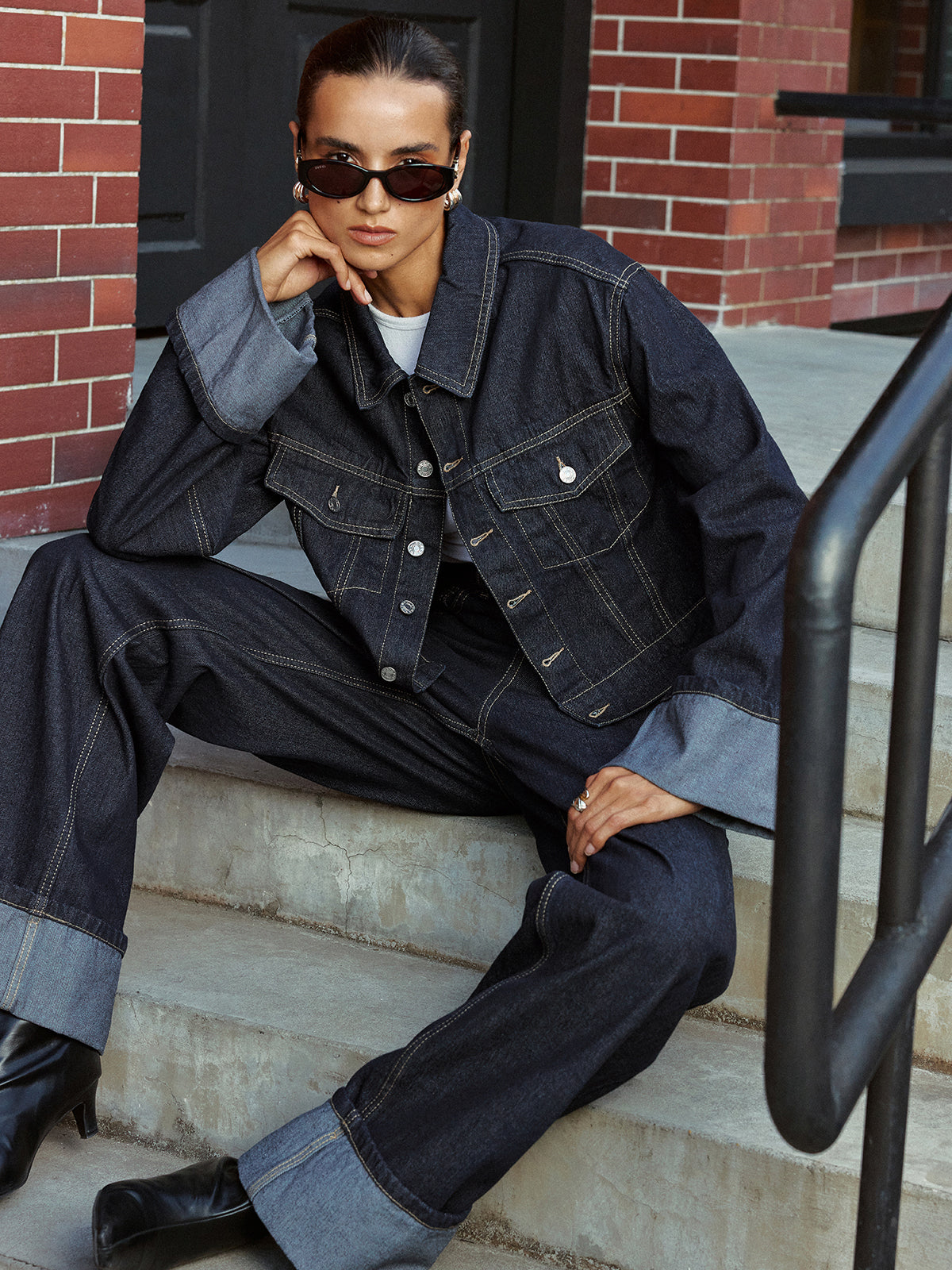 Aveline blue denim jacket with turned-back cuffs, seated on steps, front view