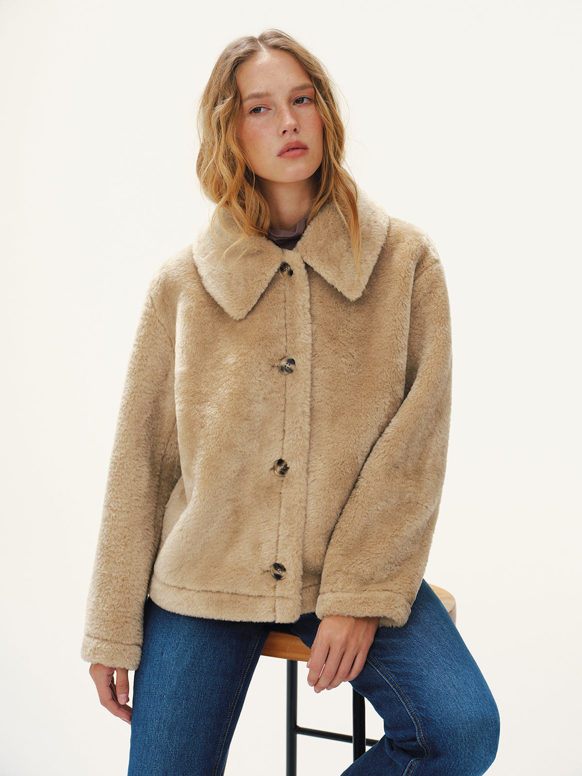 Beige plush jacket worn buttoned with jeans, seated front view