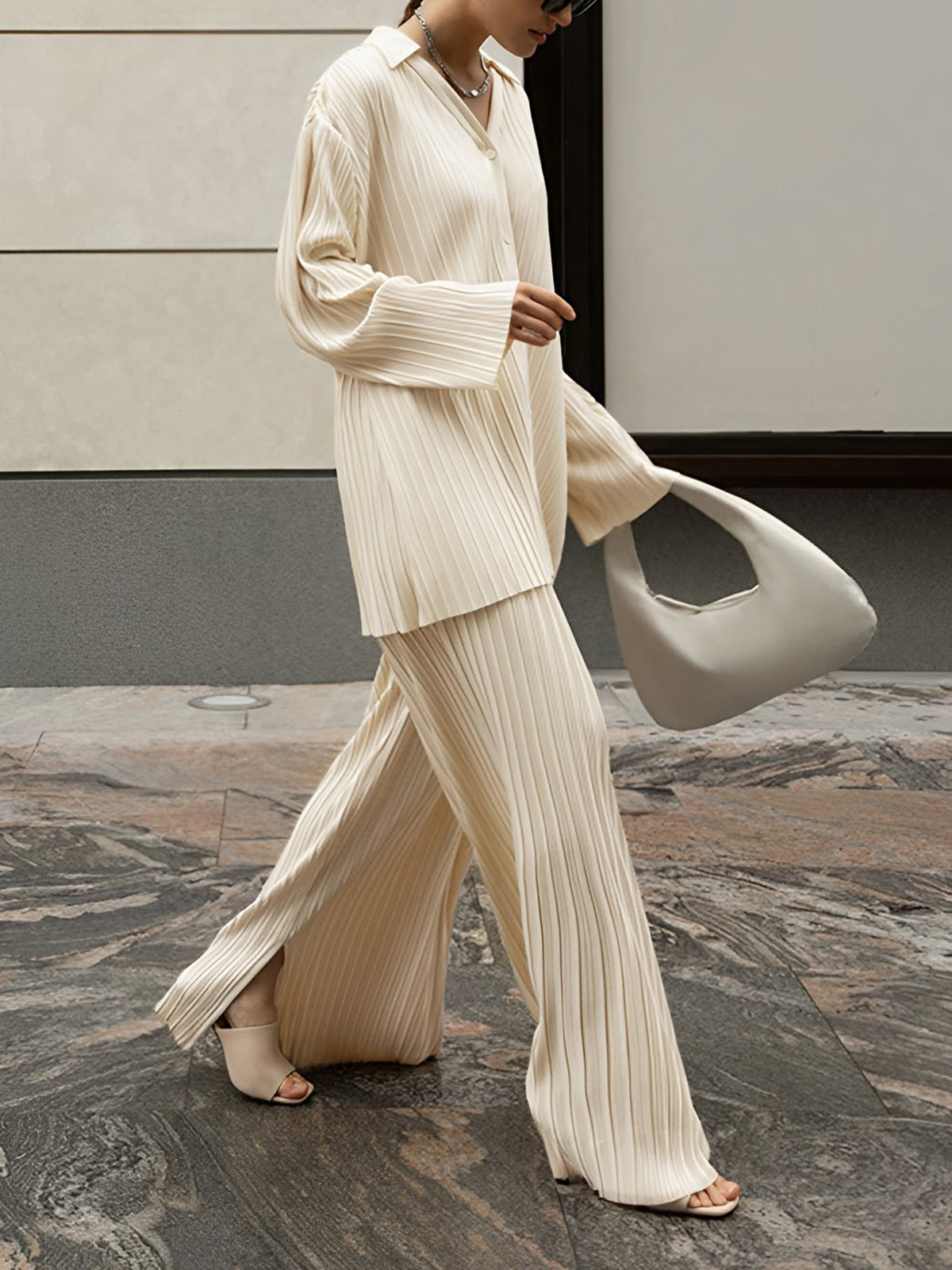 Woman wearing a cream pleated button-through shirt and matching wide-leg trousers, walking outdoors