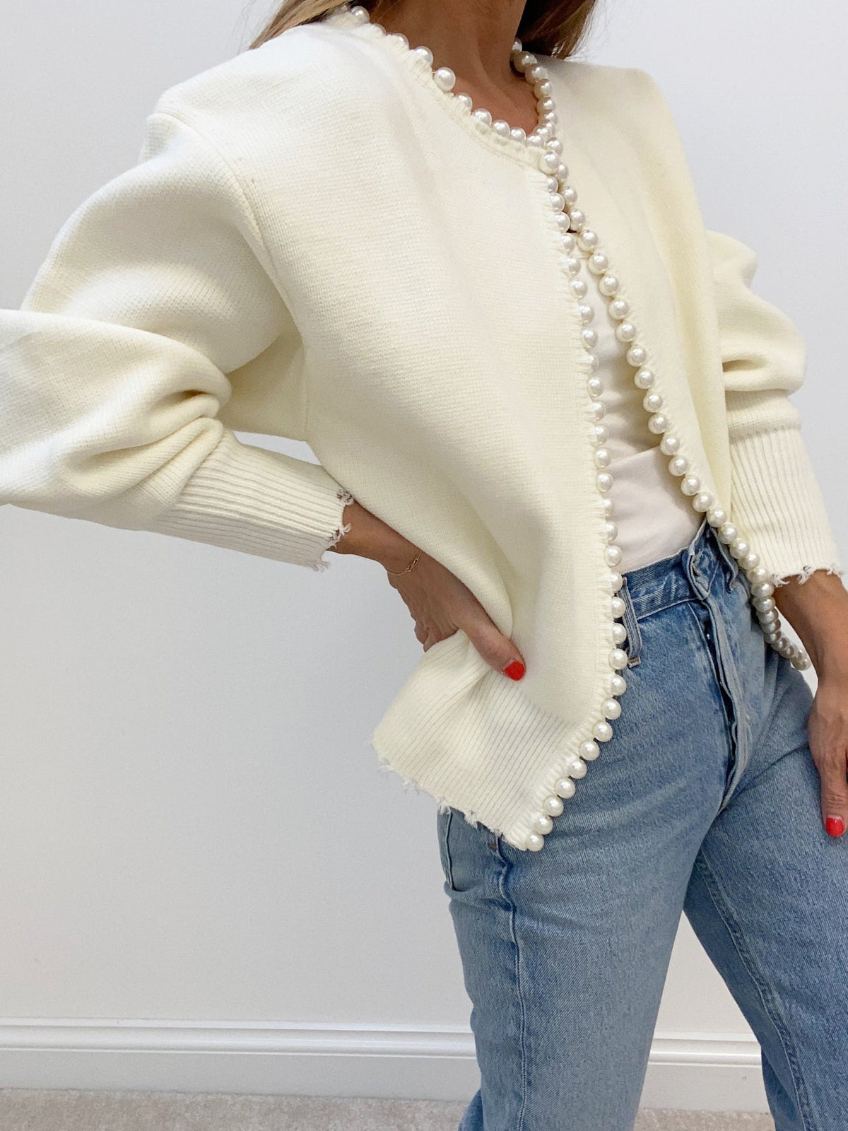 Side view of the cream pearl-trim cardigan showing the wide ribbed cuff
