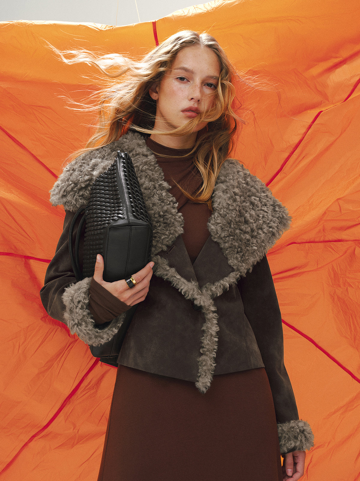 Dorothee brown faux fur trim fitted jacket worn open over a brown top, front view against an orange backdrop