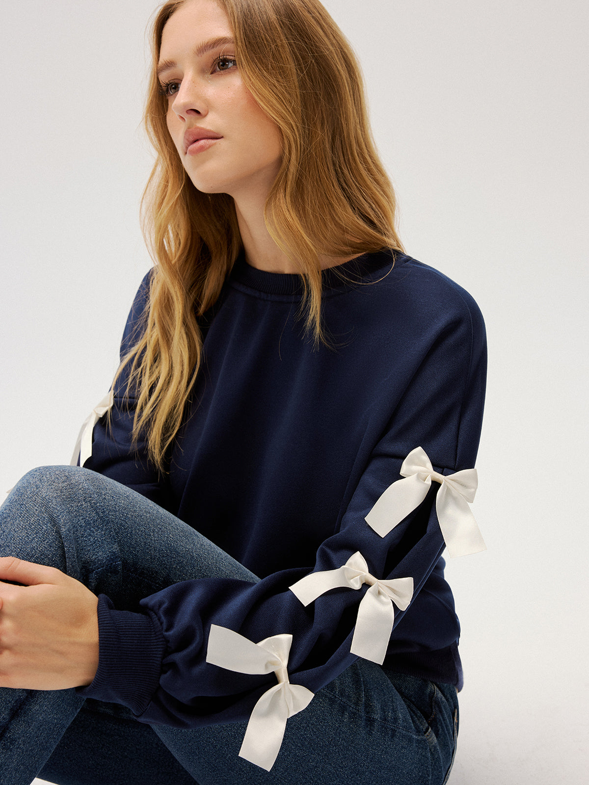 Evelyne navy ribbon bow sleeve sweatshirt, close-up of an ivory satin bow and its tails