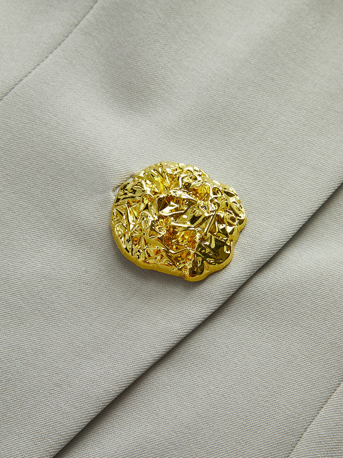 Flavie stone waistcoat, close-up of the foil-textured gold button on its thread bar loop