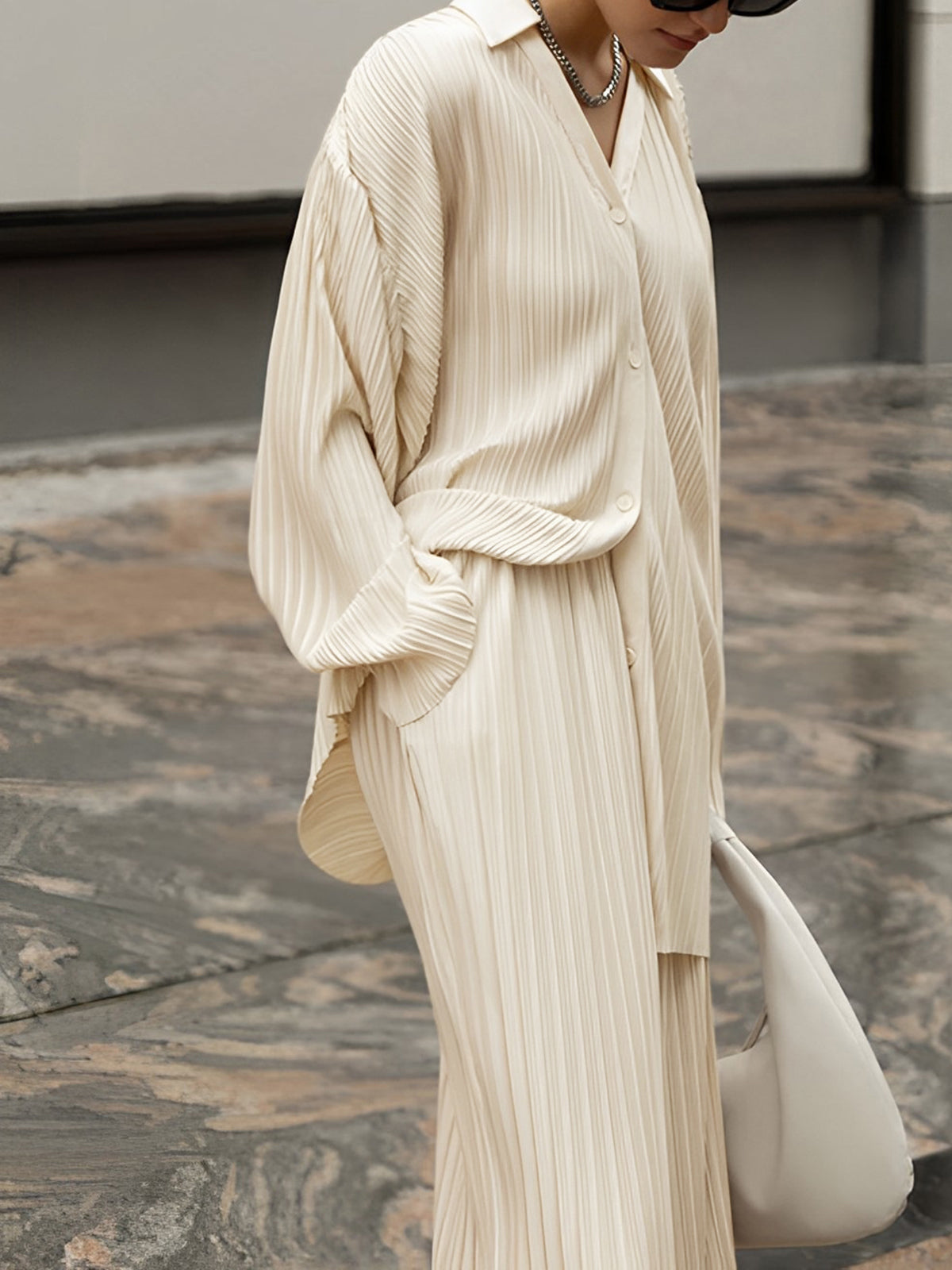 Close view of the cream pleated shirt worn open over the matching wide-leg trousers
